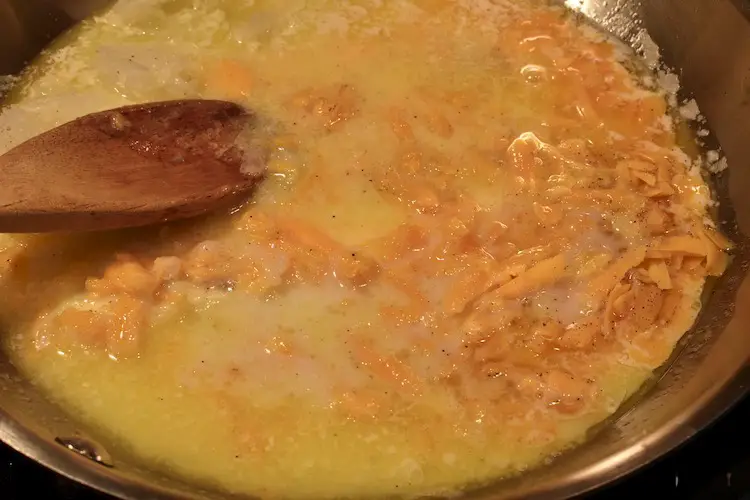 Cheddar cheese, grated onion, butter, milk, salt and pepper melting in frying pan