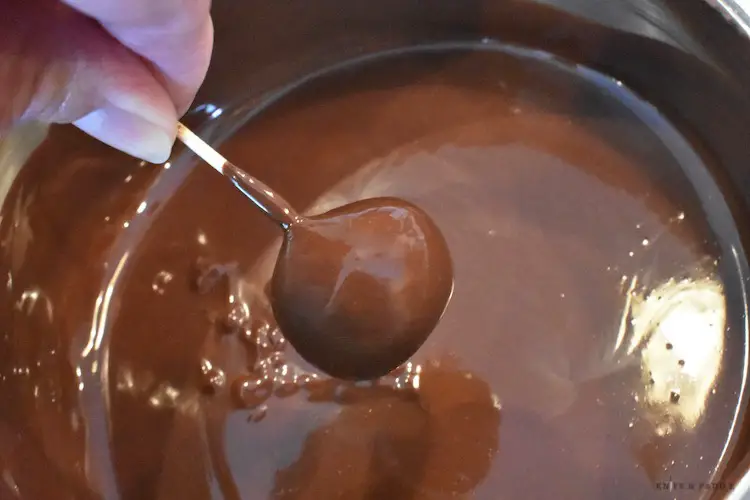 Toothpick in the center of the chilled peanut butter ball dipped in chocolate over a small saucepan