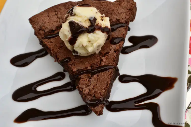 Slice of double chocolate fudge pie on a plate with a scoop of chocolate chip ice cream drizzled with chocolate sauce