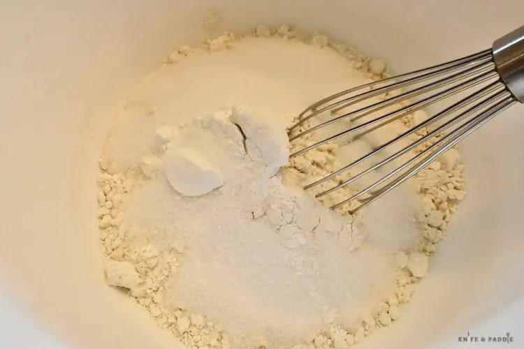 Flour, sugar, baking soda, salt in a bowl with a whisk in a mixing bowl