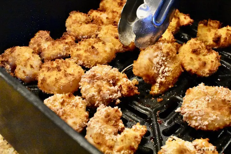 Flipping the shrimp over in the air fryer basket with tongs