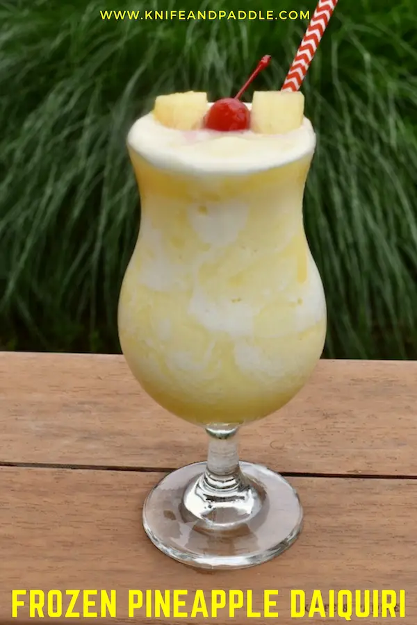 Frozen Pineapple Daiquiri in a hurricane glass garnished with two pineapple slices and a maraschino cherry