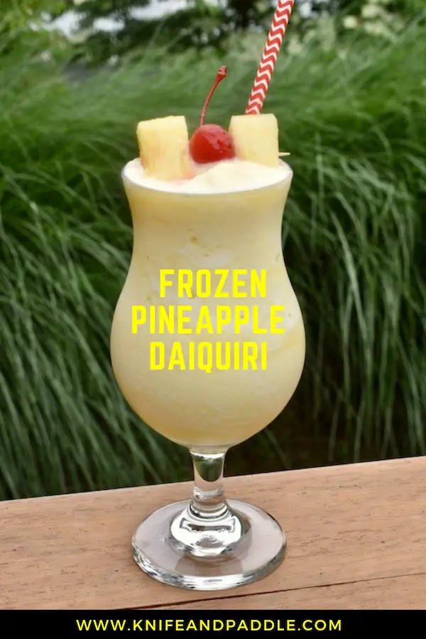 Frozen Pineapple Daiquiri in a hurricane glass garnished with two pineapple slices and a maraschino cherry