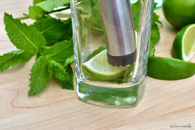 Fresh mint and lime in a glass being muddled with a muddler 