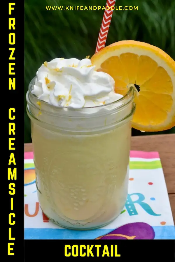 Frozen Creamsicle Cocktail in a mason jar with whipped cream and an orange slice and zest for garnish