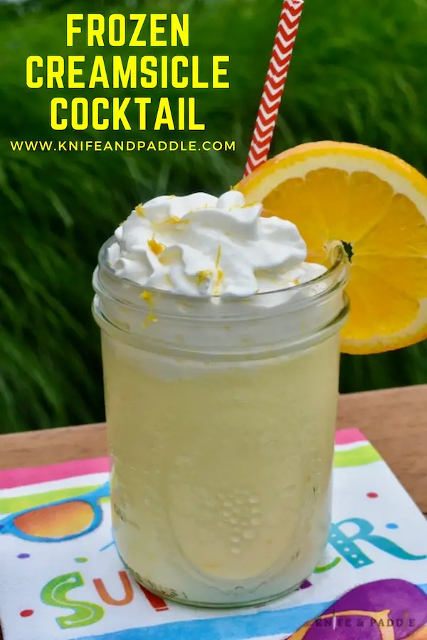 Frozen Creamsicle Cocktail in a mason jar with whipped cream and an orange slice and zest for garnish