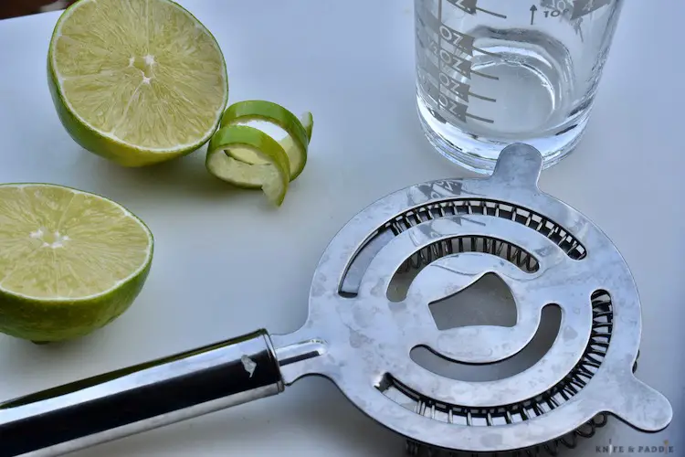 Lime, lime twist, shot glass and strainer on a cutting board