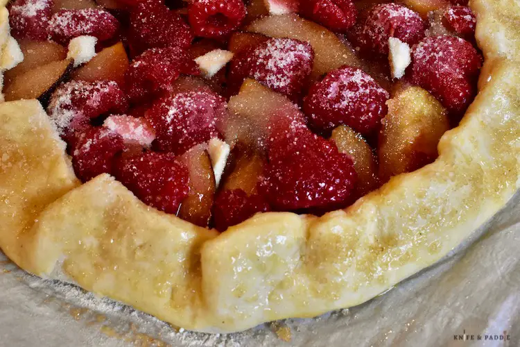 Pleated pie shell, sugar, flour, cinnamon, plums, raspberries and dotted butter, lemon juice, orange zest, egg washed edges and turbinado sugar