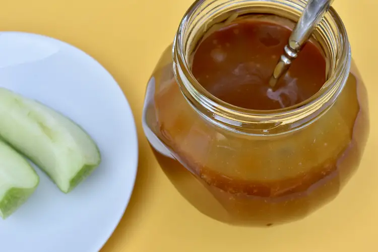 Easy Homemade Caramel Sauce in a jar with apple slices on a plate