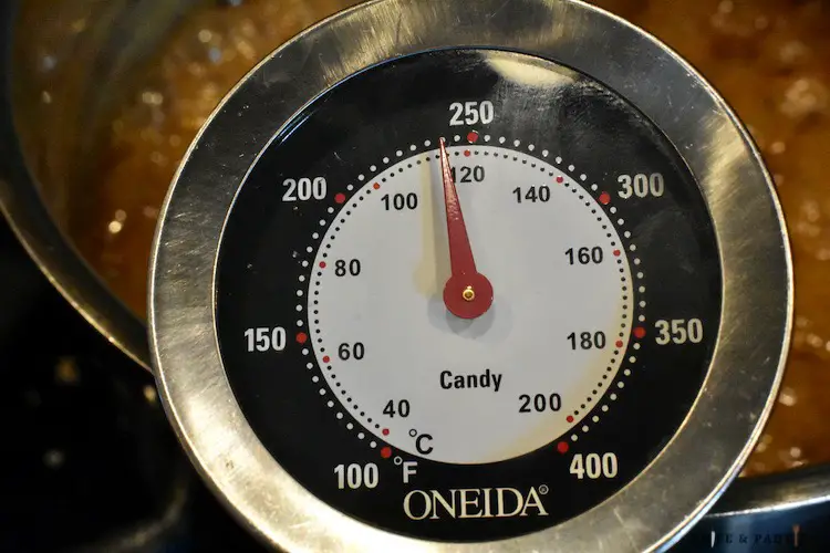 Candy thermometer inserted into boiling caramel reaching 240 degrees