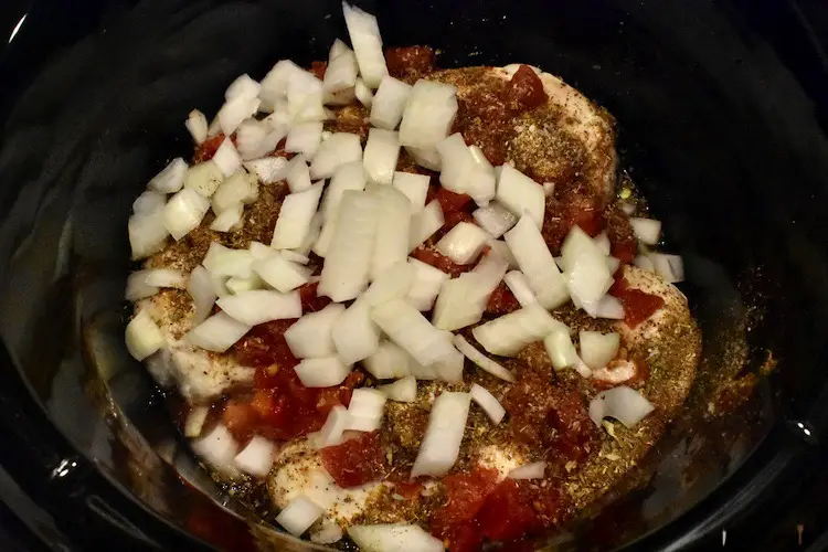 Chicken in a crockpot with diced tomatoes with green chillies and spices poured over the top