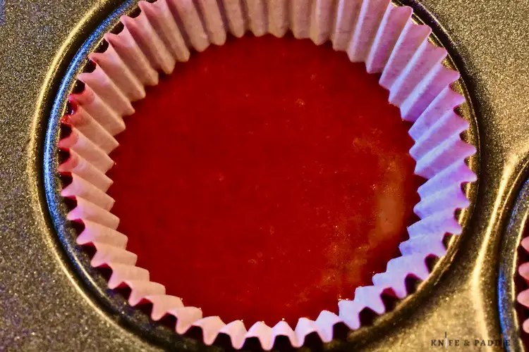 1/2 filled liner with red batter in a muffin tin