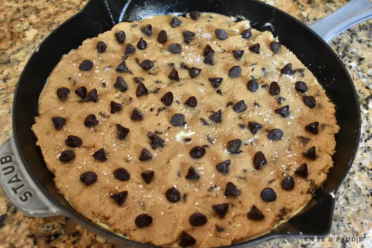 Cookie dough in a cast iron pan topped with chocolate chips and Kosher salt