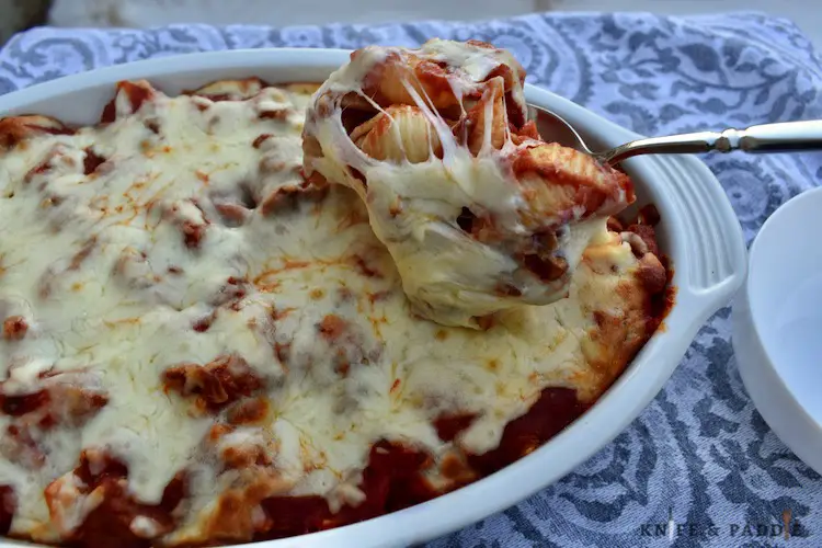 Scooping shells, tomato sauce, sausage and cheese from an oven safe dish