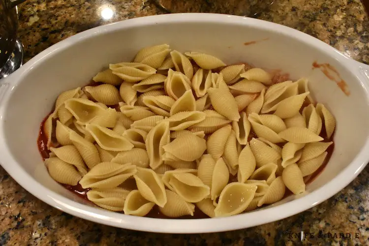 Mushrooms, onions and tomato sauce on the bottom of a large casserole dish topped with cooked shell pasta