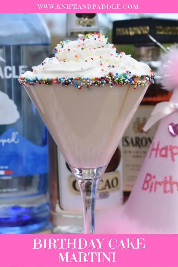 Birthday Cake Martini with whipped cream and rainbow nonpareils in a martini glass rimmed with fluff and rainbow nonpareils