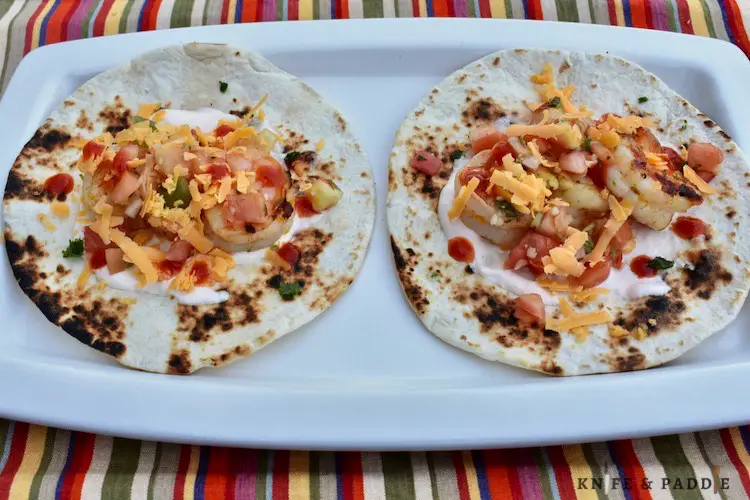 Grilled shrimp tacos with sour cream, salsa, sriracha and cheddar cheese on a toasted tortilla 