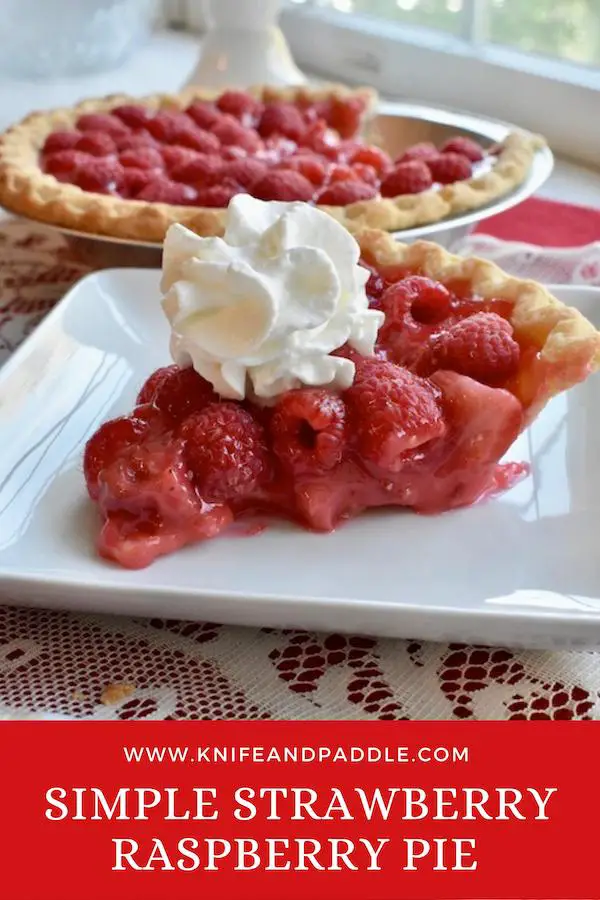Slice of strawberry raspberry pie on a pie plate with whipped cream