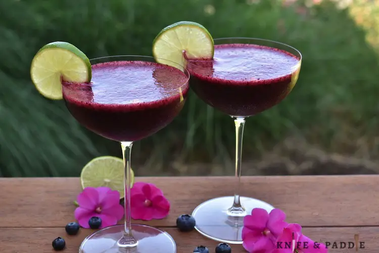 Blueberries, rum, simple sugar, fresh squeezed lime juice and ice in cocktail glasses with a lime slice