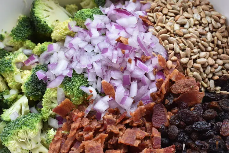 Broccoli, diced purple onion, sunflower seeds, chopped bacon and raisins in a mixing bowl