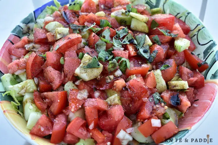 Iceberg lettuce, tomatoes, cucumbers, onions, olive oil, basil, bread and balsamic mixed in a bowl