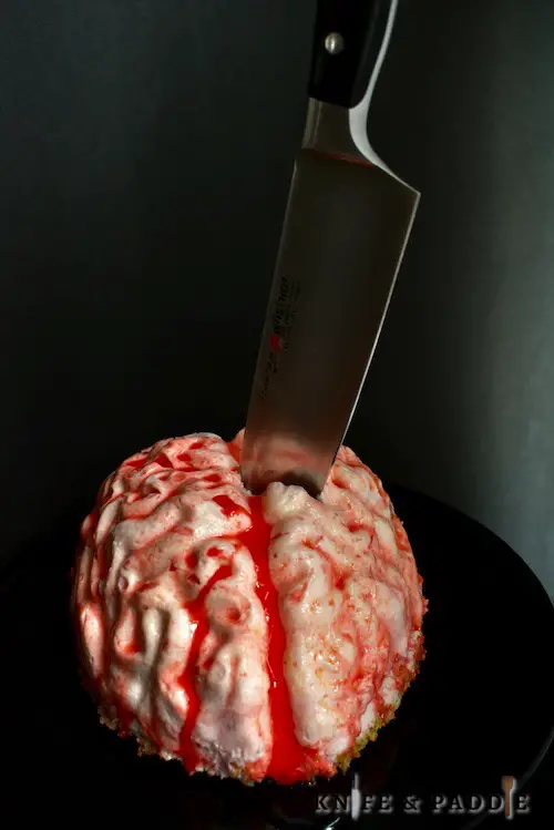 No-Bake Cheesecake Brain with strawberry sauce on a plate with a butcher knife stabbed into the brain