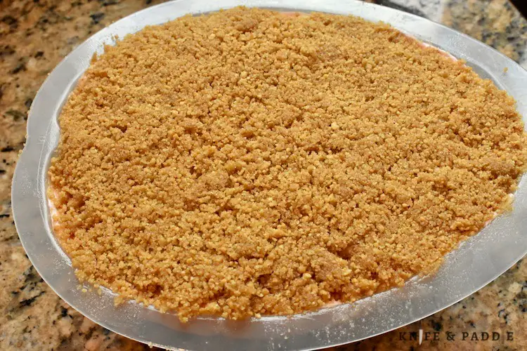 Cream cheese, sugar, gelatin, water, pure vanilla extract, pinch of salt, lemon juice, heavy whipping cream and red food coloring combined and spread in a mold with fresh strawberry filling in the center and topped with graham cracker crumbs