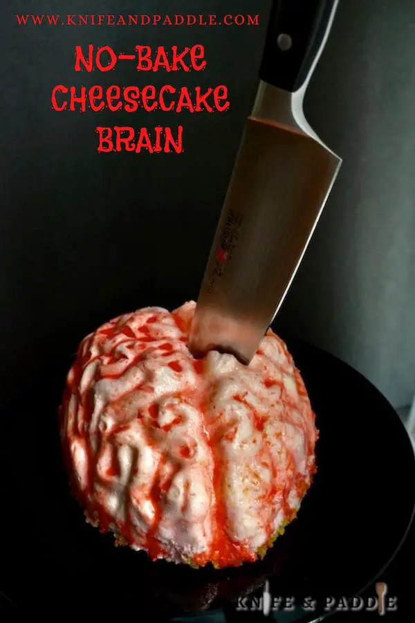 No-Bake Cheesecake Brain with strawberry sauce on a plate with a butcher knife stabbed into the brain