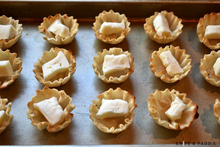 Phyllo shells on a baking sheet with a small piece of cheese in the center