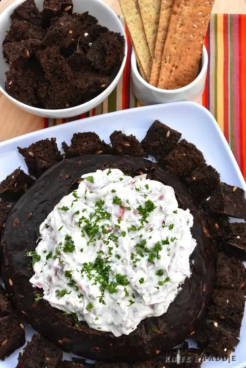 Rye Bread Beef Dip served in a pumpernickel bread bowl topped with parsley and served with crackers and rye bread chunks