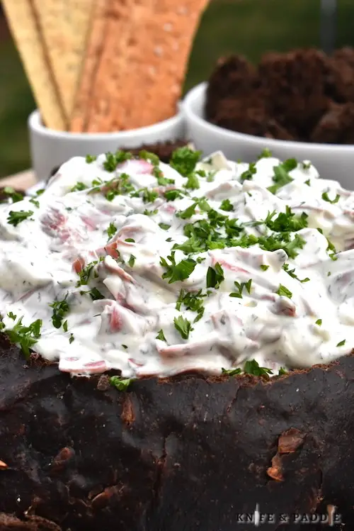 Rye Bread Beef Dip served in a pumpernickel bread bowl topped with parsley and served with crackers and rye bread chunks