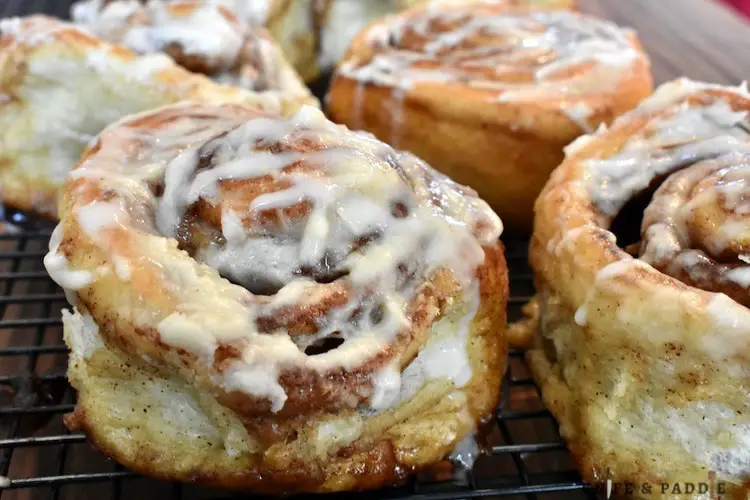 Baked golden brown cinnamon buns with vanilla frosting on a wire rack