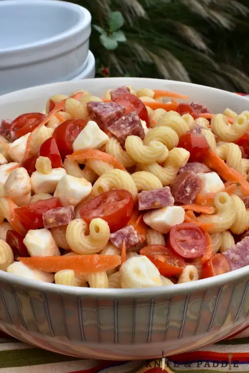 chopped hard salami, mozzarella balls, shredded carrots, grape tomatoes, cavatappi and zesty dressing in a serving bowl