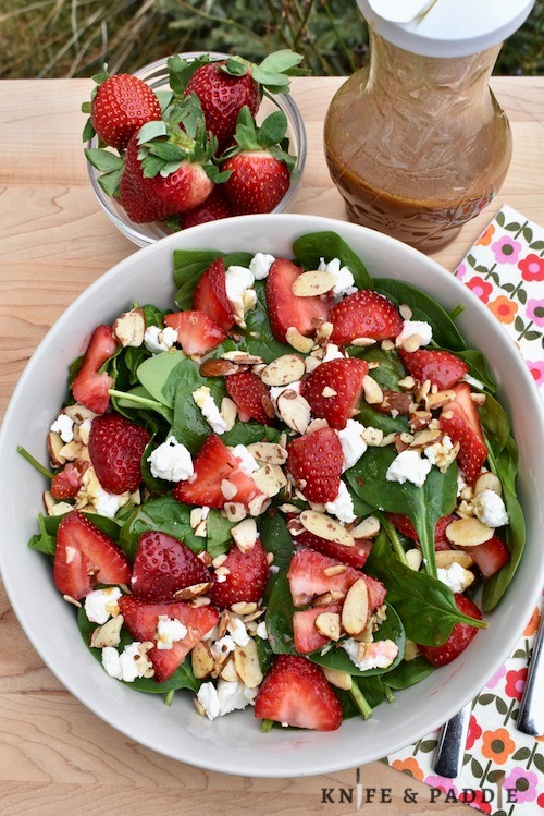 Strawberry Spinach Salad in a bowl with goat cheese crumbles and honey roasted sliced almonds drizzled with homemade balsamic dressing 