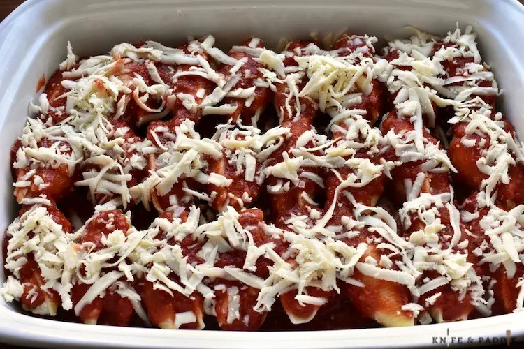 Pasta filled with ricotta, mozzarella, and parmesan cheese placed in a baking dish smothered with sauce and fresh, grated mozzarella cheese