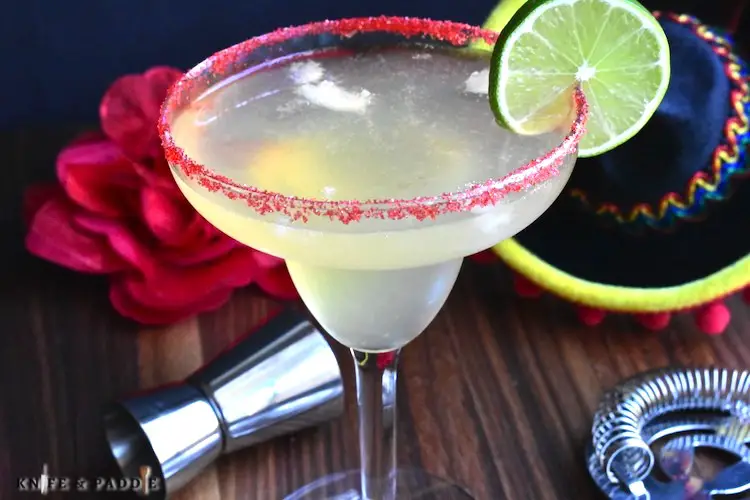 Fireball margarita poured into a margarita glass rimmed with red sparkling sugar and garnished with a lime slice