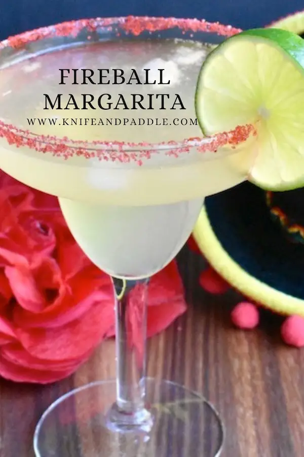 Fireball margarita poured into a margarita glass rimmed with red sparkling sugar and garnished with a lime slice
