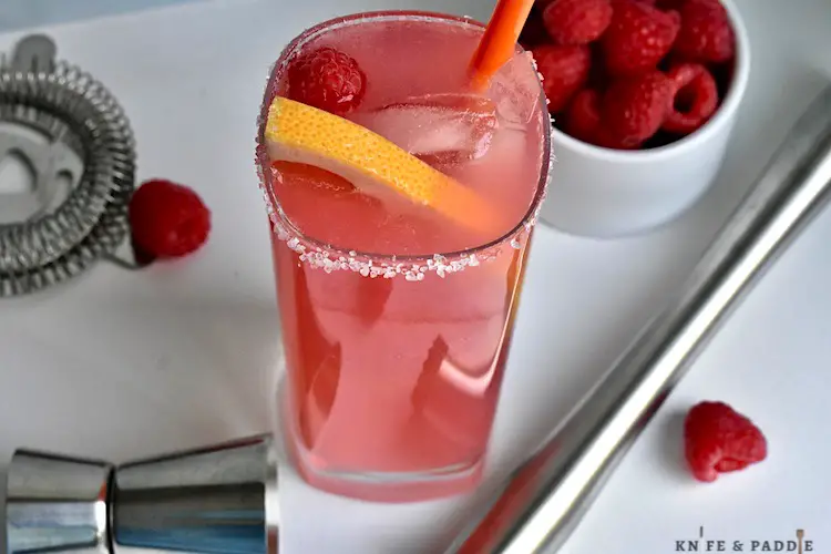 Refreshing Raspberry Paloma with a salted rim and garnished with a grapefruit slice and raspberry served in a high ball glass with ice