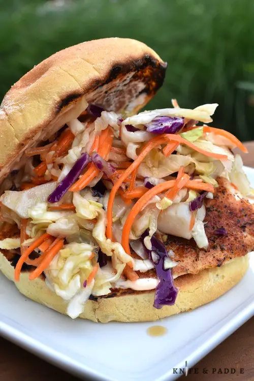 Toasted bulkie roll with spicy mayonnaise, topped with blackened sole and a mixture of red and green cabbage, shredded carrots mixed in a rice wine vinegar, honey, sesame oil and soy sauce served on a plate