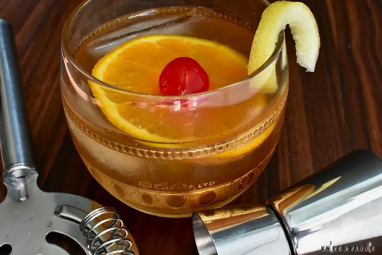 Amaretto Sour Cocktail in a rocks glass garnished with a lemon twist, orange slice and maraschino cherry