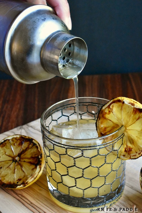 Pouring a Grilled Whiskey Sour with grilled lemons and a grilled lemon wheel for garnish