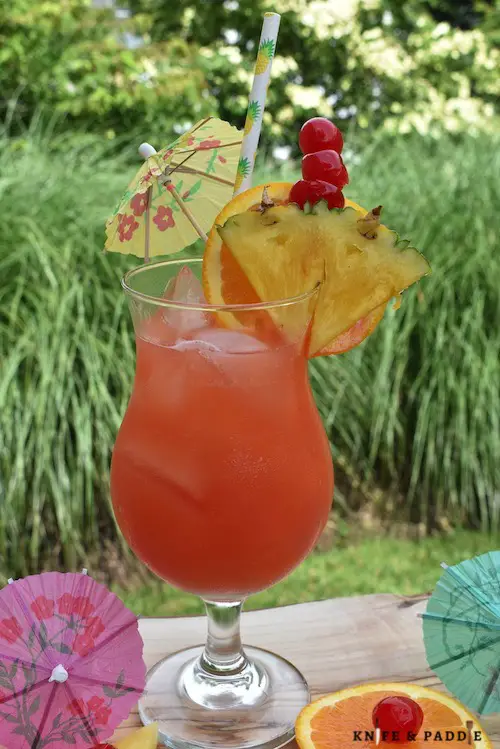 Refreshing, fruity summer cocktail in a hurricane glass garnished with a pineapple slice, orange slice and a cocktail umbrella
