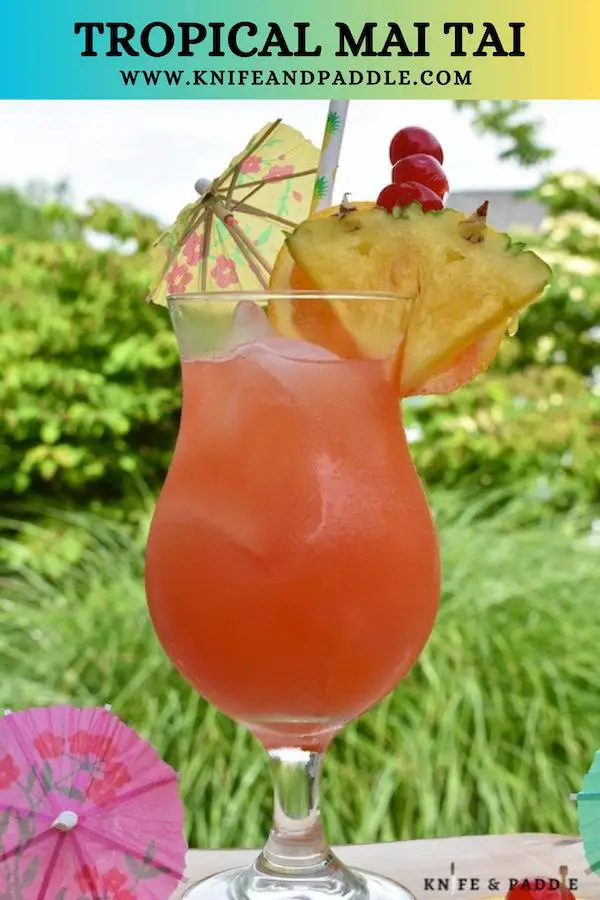 Tropical Mai Tai in a hurricane glass garnished with a pineapple slice, orange slice, maraschino cherries and a cocktail umbrella