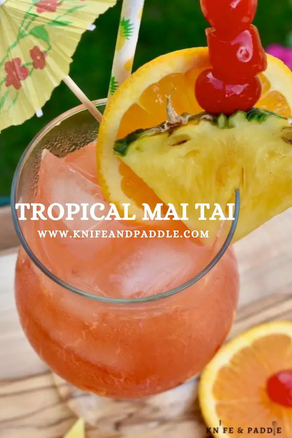 Tropical Mai Tai in a hurricane glass garnished with a pineapple slice, orange slice, maraschino cherries and a cocktail umbrella