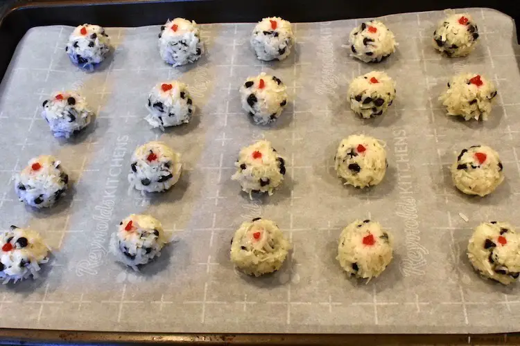 Coconut balls with a piece of maraschino cherry on the top placed on a parchment lined baking sheet