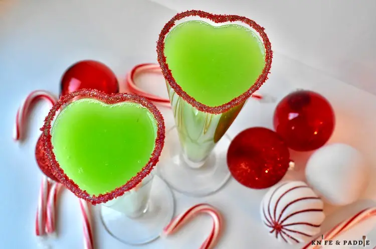 Grinch Mimosa in a heart shaped champagne glass rimmed with red sparkling sugar