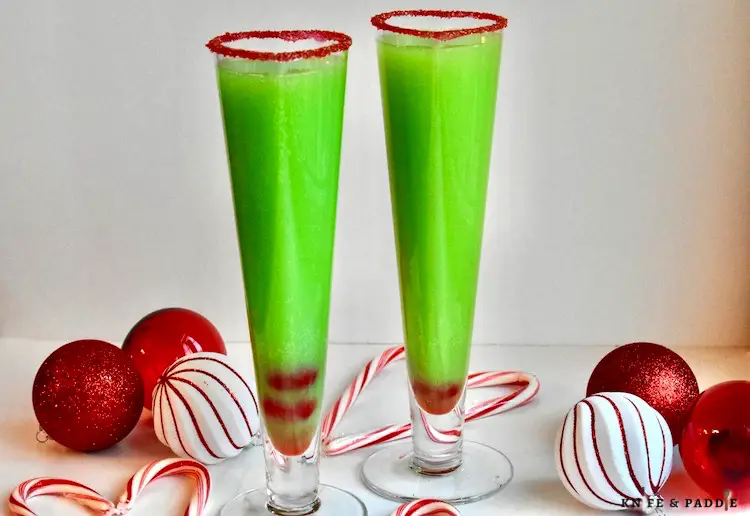 Festive bright green Christmas Cocktail in a heart shaped champagne glass rimmed with red sparkling sugar and garnished with two maraschino cherries in the bottom of the glass