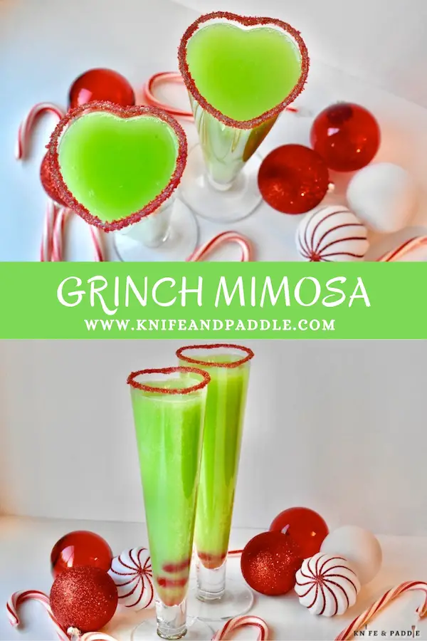 Bright green Grinch Mimosa in a heart shaped champagne glass rimmed with red sparkling sugar and two maraschino cherries in the bottom of the glass