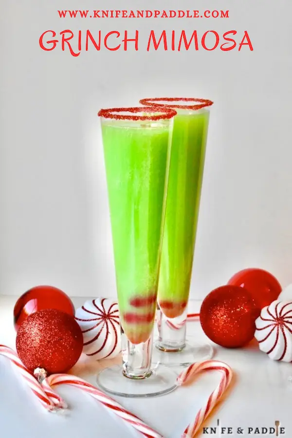 Festive bright green Christmas Cocktail in a heart shaped champagne glass rimmed with red sparkling sugar and garnished with two maraschino cherries in the bottom of the glass