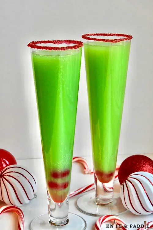 Bright green Grinch Mimosa in a heart shaped champagne glass rimmed with red sparkling sugar